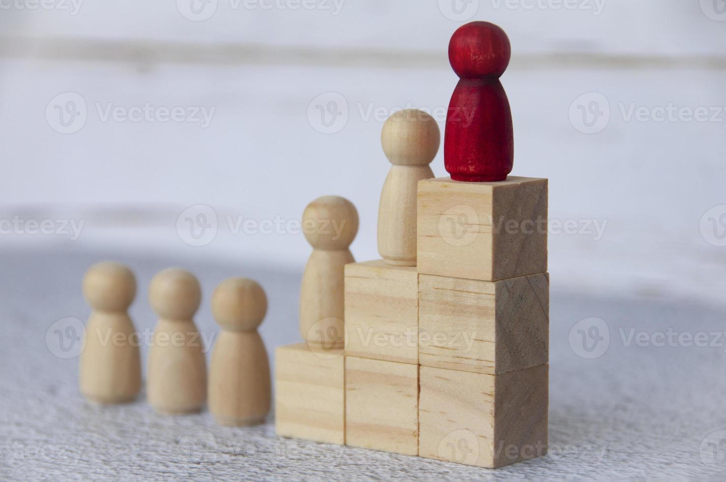 Wooden people figures on top of wooden blocks with red figure leading the rest. Business concept photo