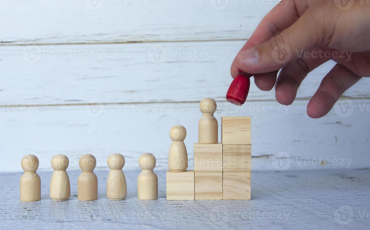Wooden people figures on top of wooden blocks with hand holding red figure doll. Business concept photo