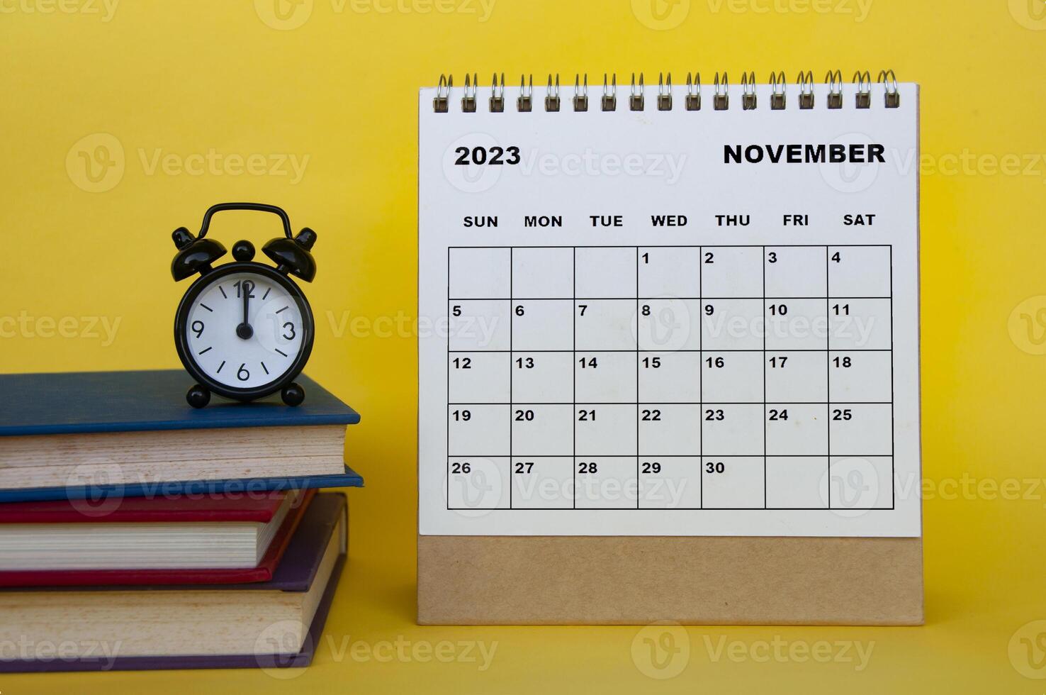 November 2023 desk calendar with books and alarm clock on yellow background. photo