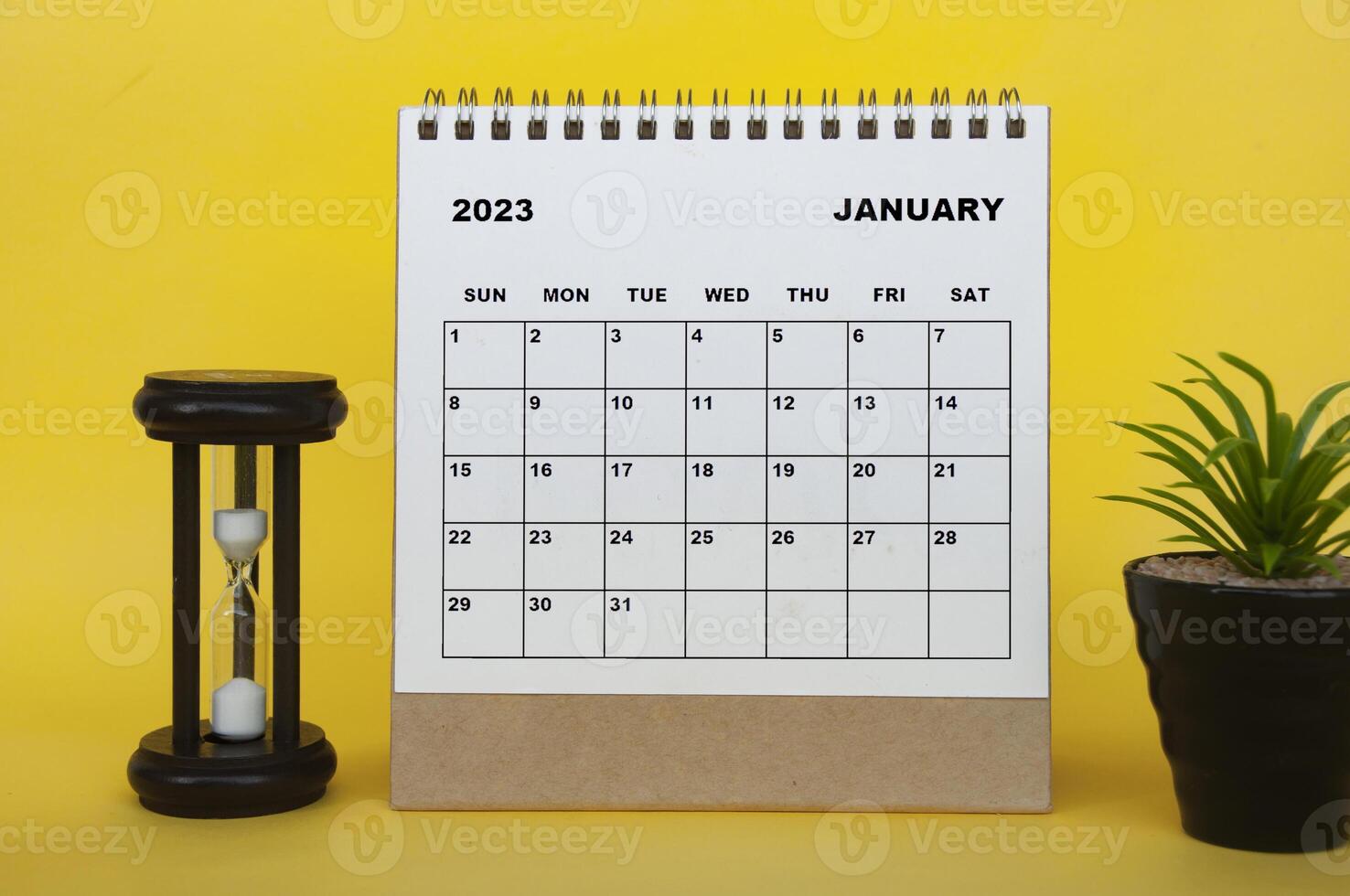 January 2023 desk calendar with table plant and minutes glass on yellow background. photo