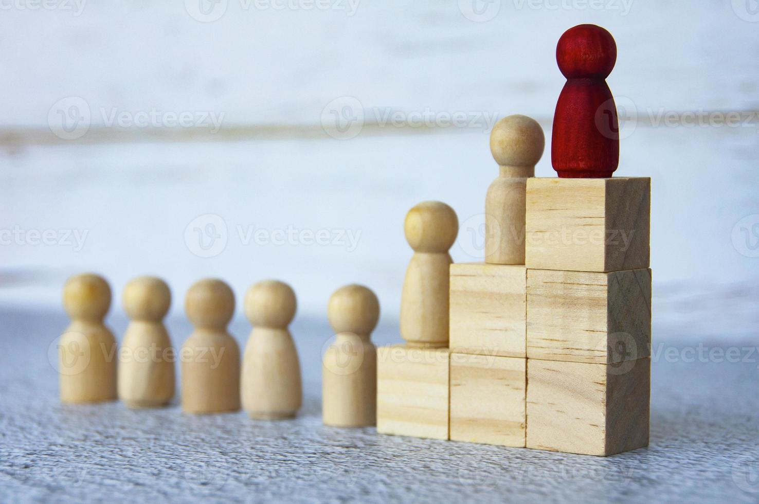 Wooden people figures on top of wooden blocks with red figure leading the rest. Business concept photo