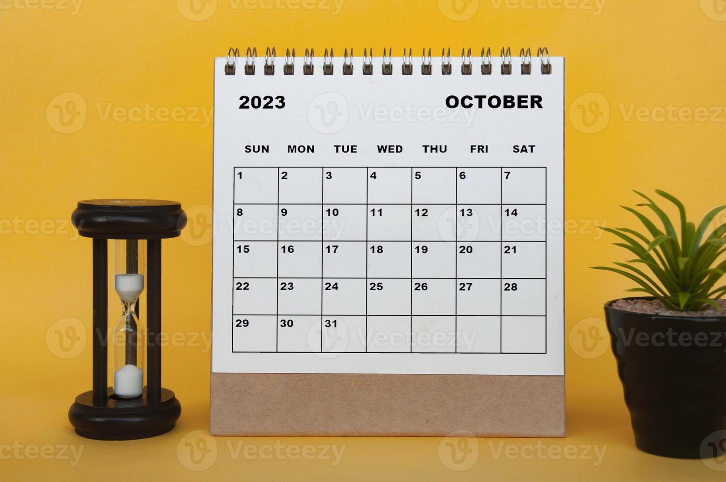 calendario de escritorio de octubre de 2023 con vidrio de minutos y planta sobre fondo amarillo. foto