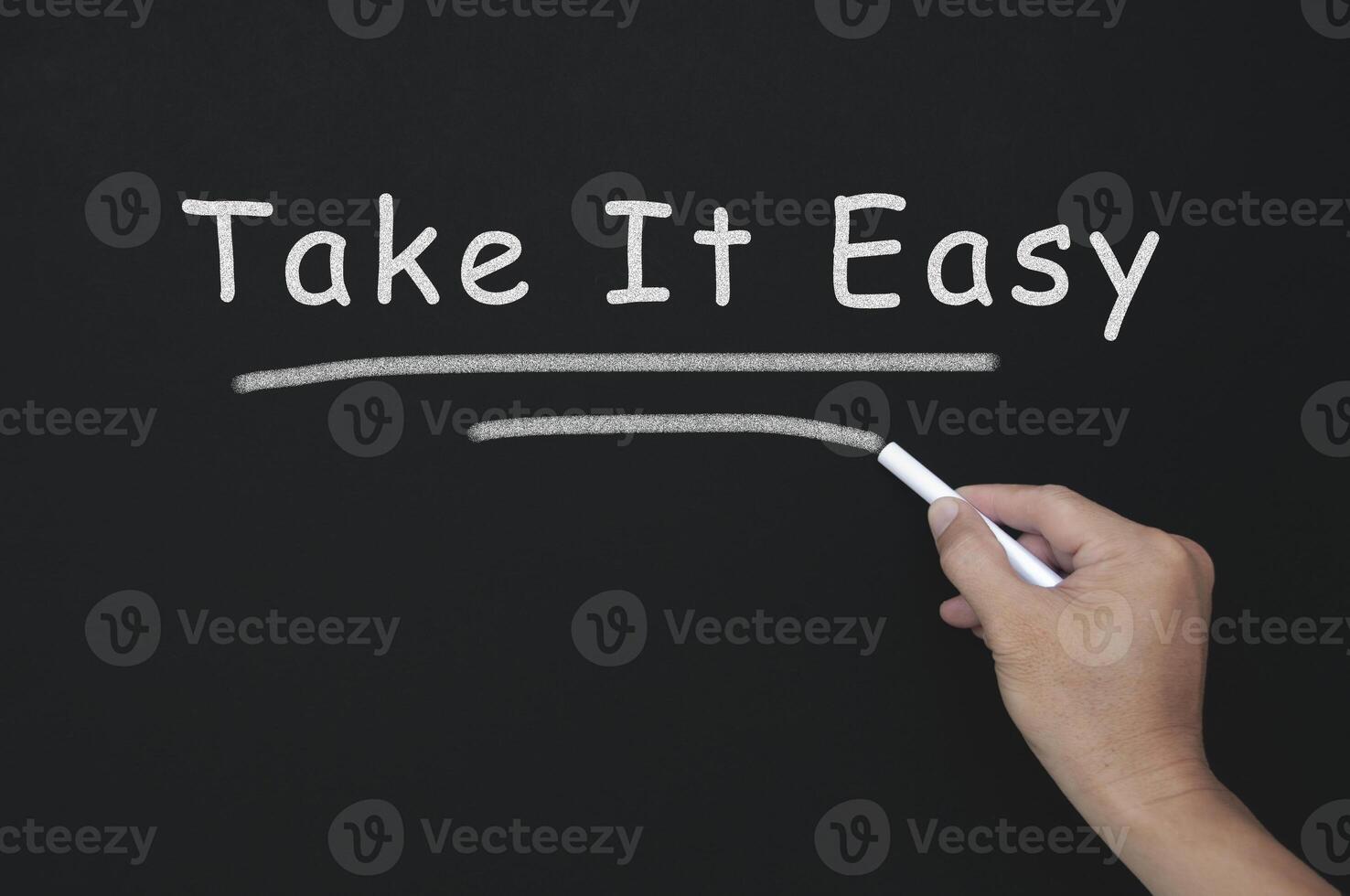 Take it easy text on blackboard with hand holding chalk. photo