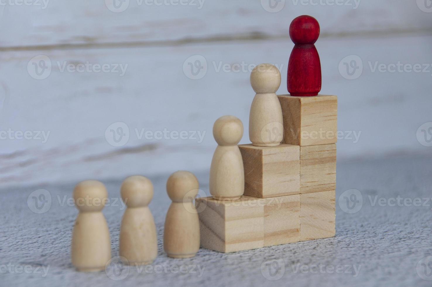Wooden people figures on top of wooden blocks with red figure leading the rest. Business concept photo
