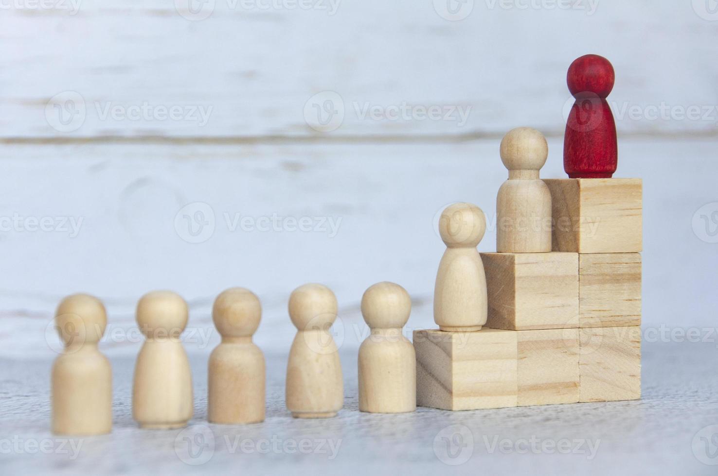 Wooden people figures on top of wooden blocks with red figure leading the rest. Business concept photo