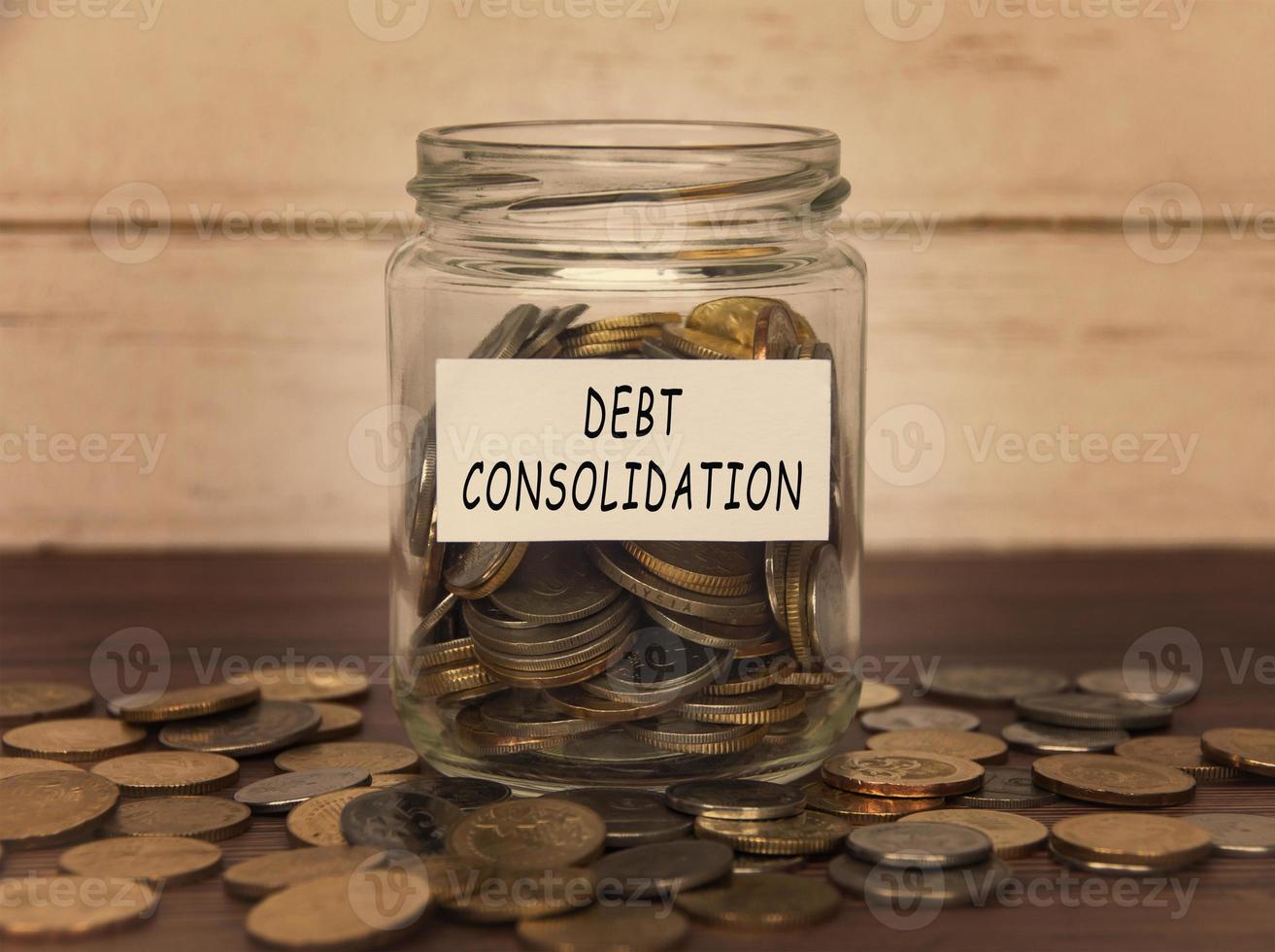 Debt consolidation label on coin jar on top of wooden desk with asorted coins background. photo