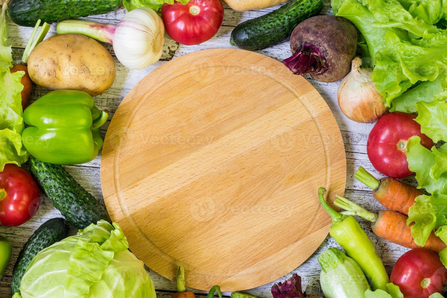 tabla de cortar circular y verduras sobre fondo blanco de madera. alimentación saludable foto