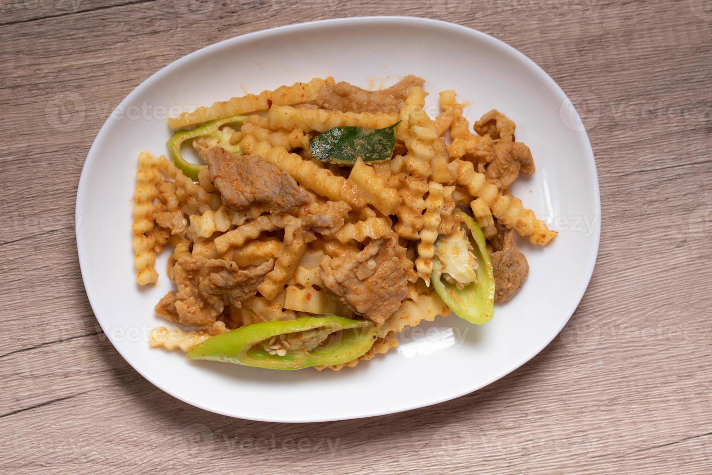 Stir-fried pork with red curry paste and young coconut shoots in a white plate photo