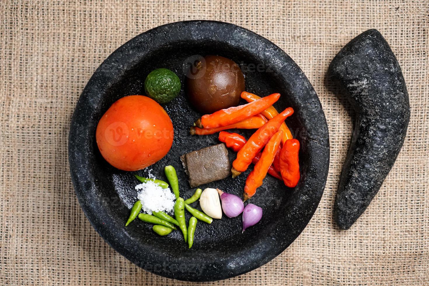 top view of mortar and pestle with ingredients for chili sauce, shallots, onion, tomatoes, cayenne, terasi, palm sugar, lemon photo