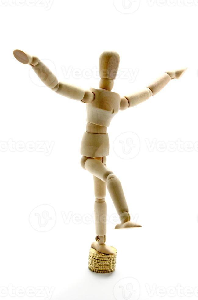 Wooden mannequin balancing over coins photo