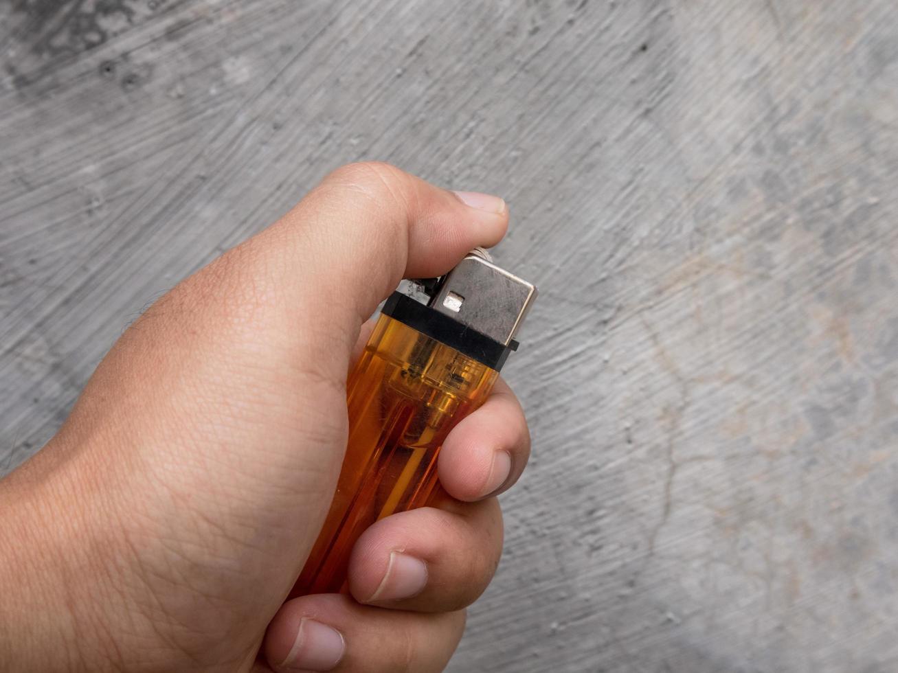 a man tries to light an orange gas lighter in his hand photo