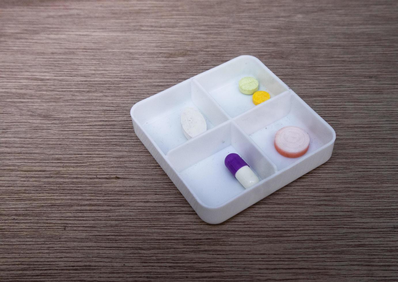 Close-up photo of various medicines in one white container isolated on the background on a wooden board