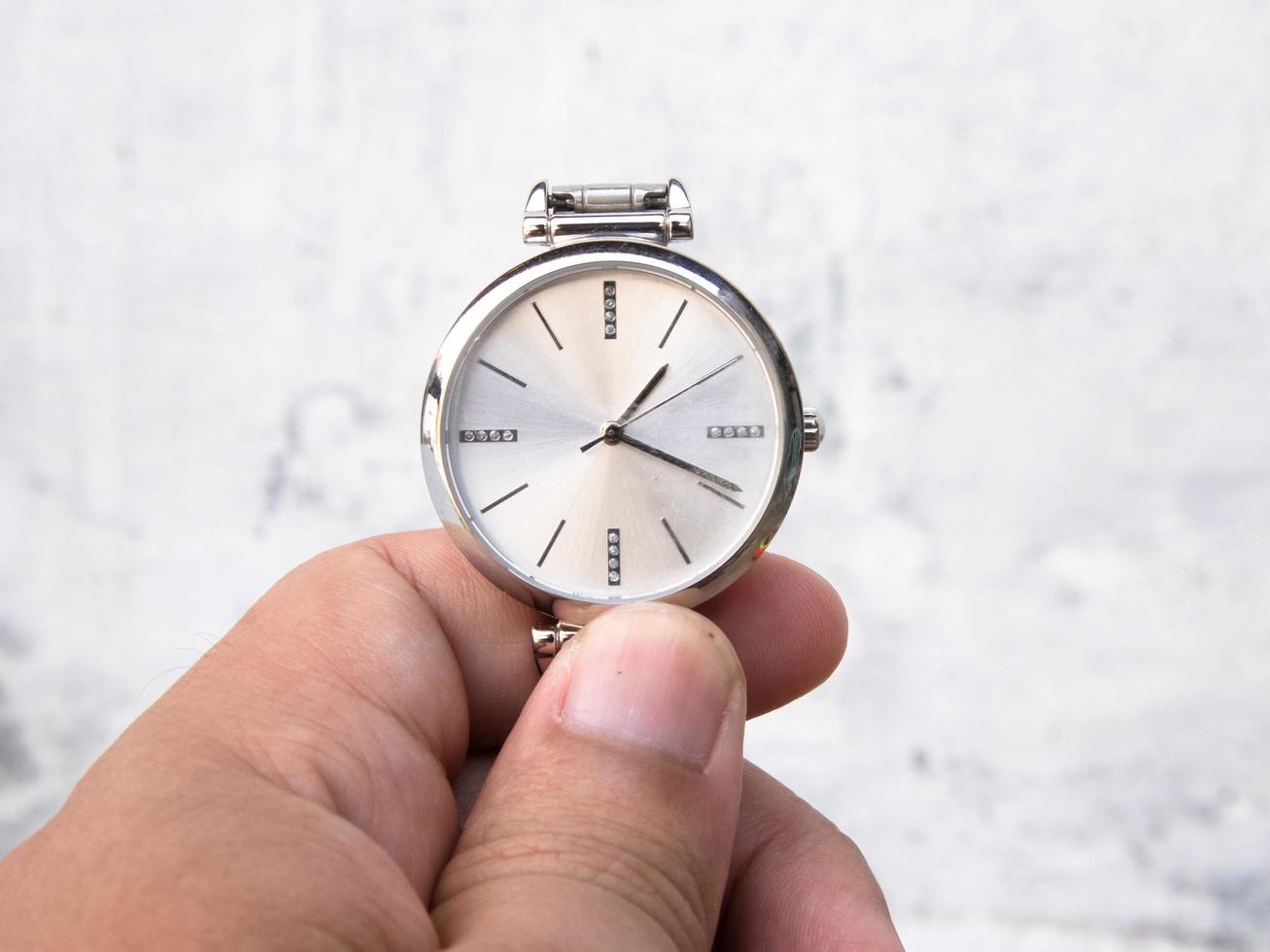 a man holds a watch by holding the end of the watch strap photo