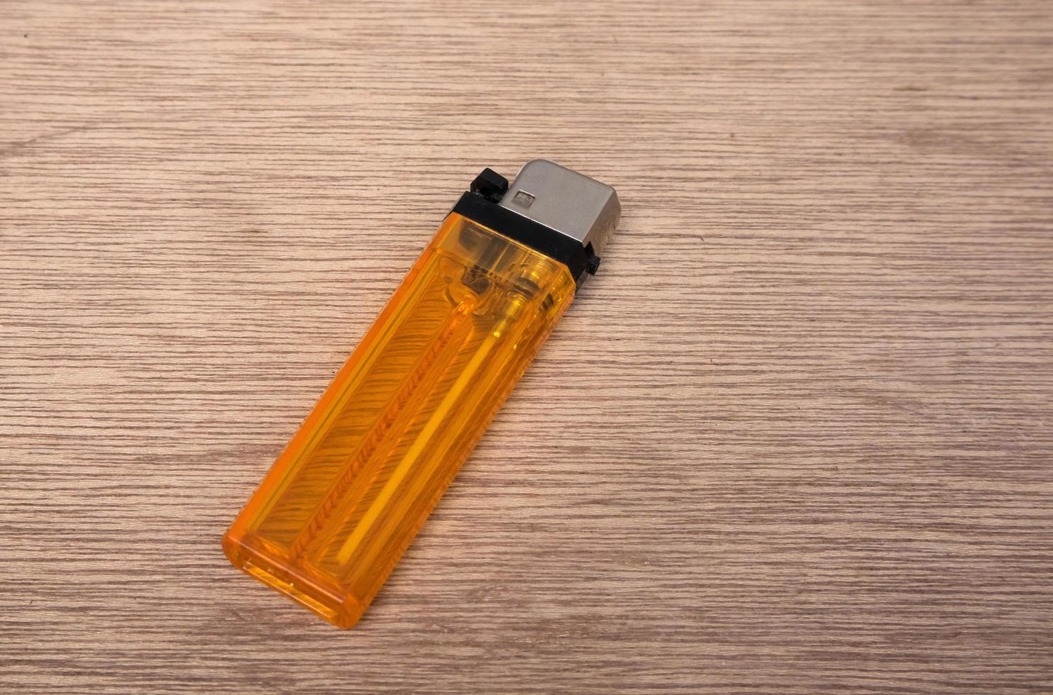 foto de primer plano de un encendedor de gas naranja transparente aislado sobre un fondo en una tabla de madera
