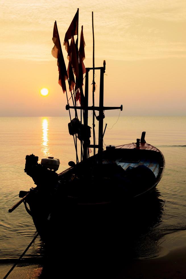 Silhouette of a fishing boat bound on a beach with sunrise in the morning, fresh orange sky. photo