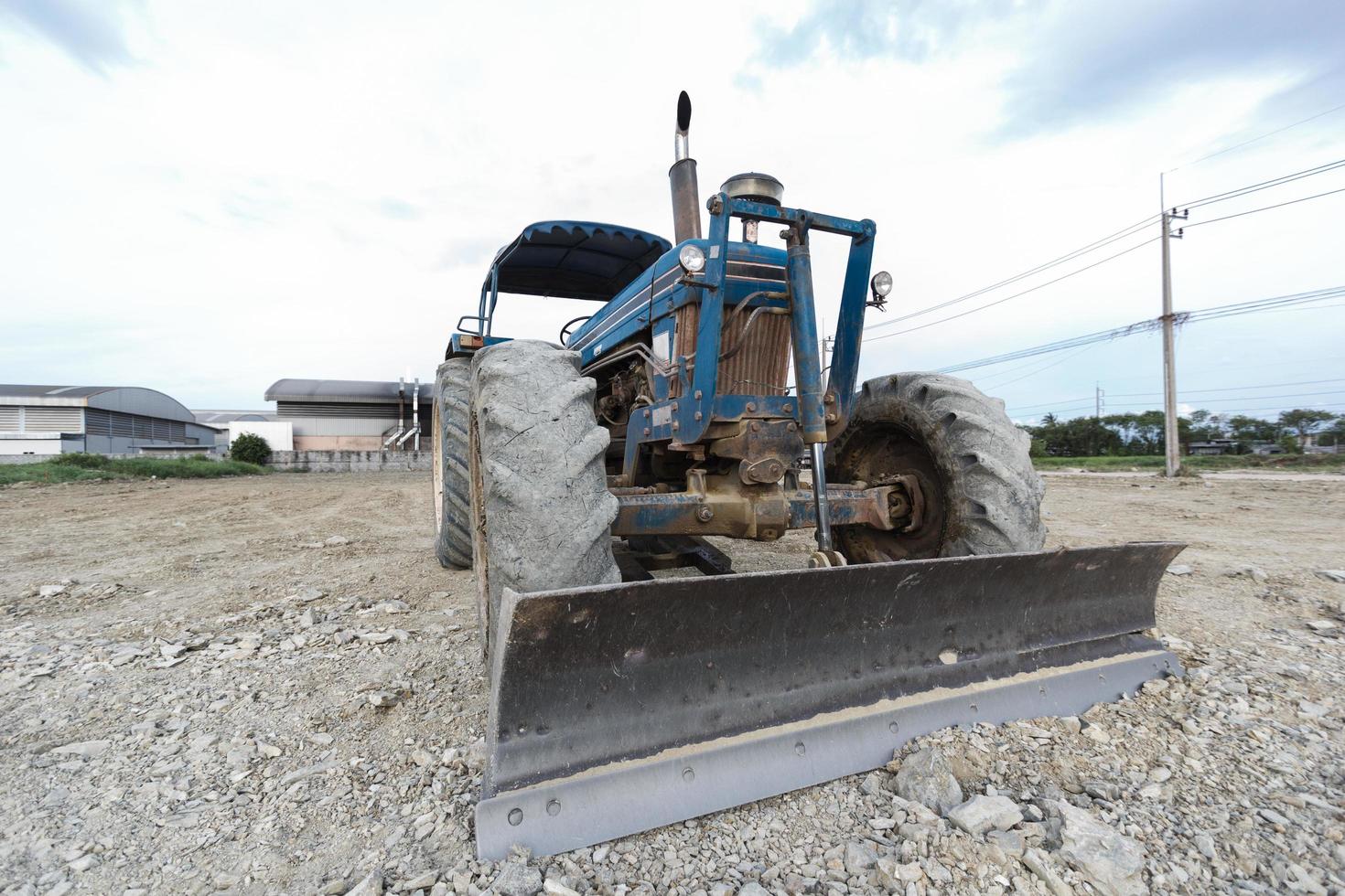 tractor azul estacionado en un claro en preparación para la capa superior del suelo y un hermoso cielo azul en el fondo. el concepto de una excavadora prepara la capa superior del suelo para la construcción. foto