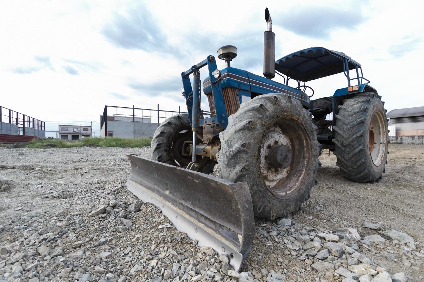 tractor azul estacionado en un claro en preparación para la capa superior del suelo y un hermoso cielo azul en el fondo. el concepto de una excavadora prepara la capa superior del suelo para la construcción. foto