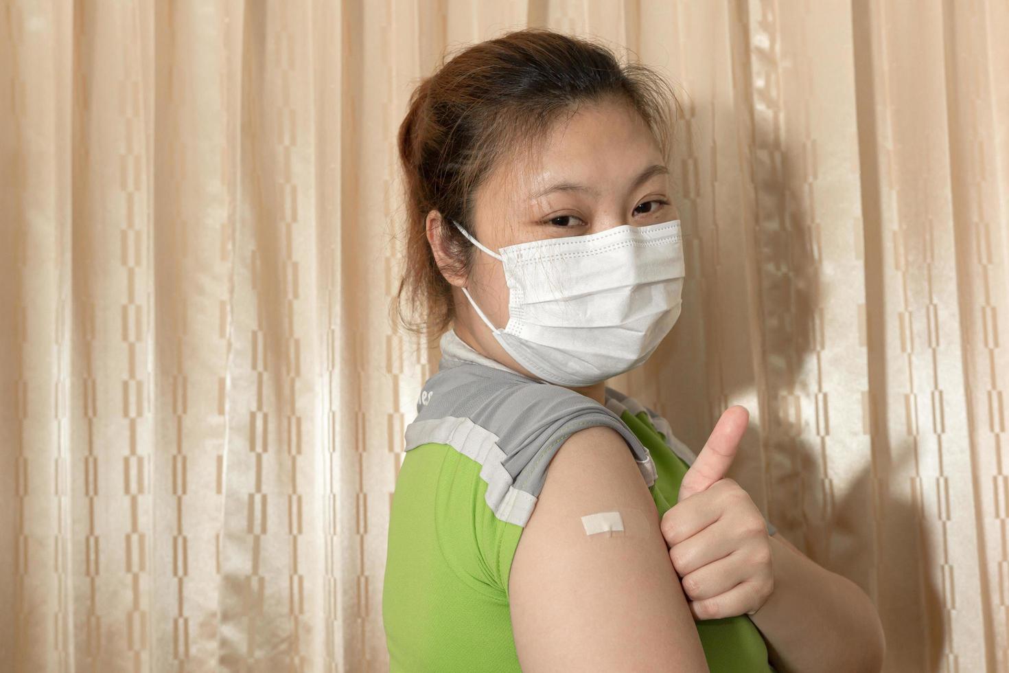 Asian woman wearing a mask, showing plaster on her arm after vaccination against COVID-19, coronavirus vaccination concept. photo