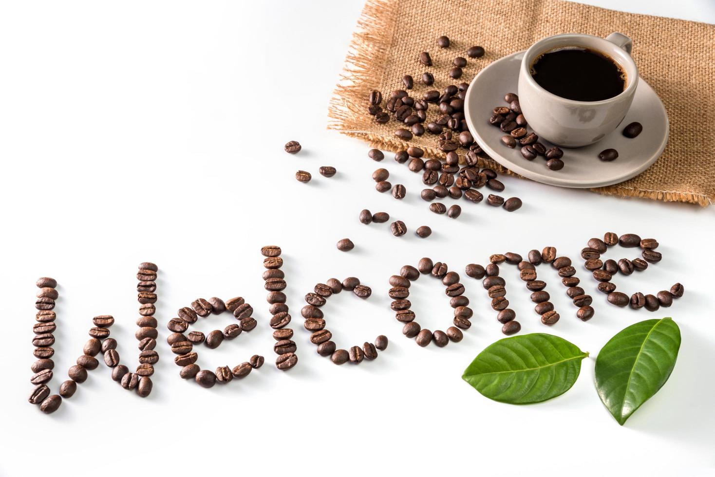 taza de café y texto de bienvenida hechos de granos de café, aislados en blanco. foto
