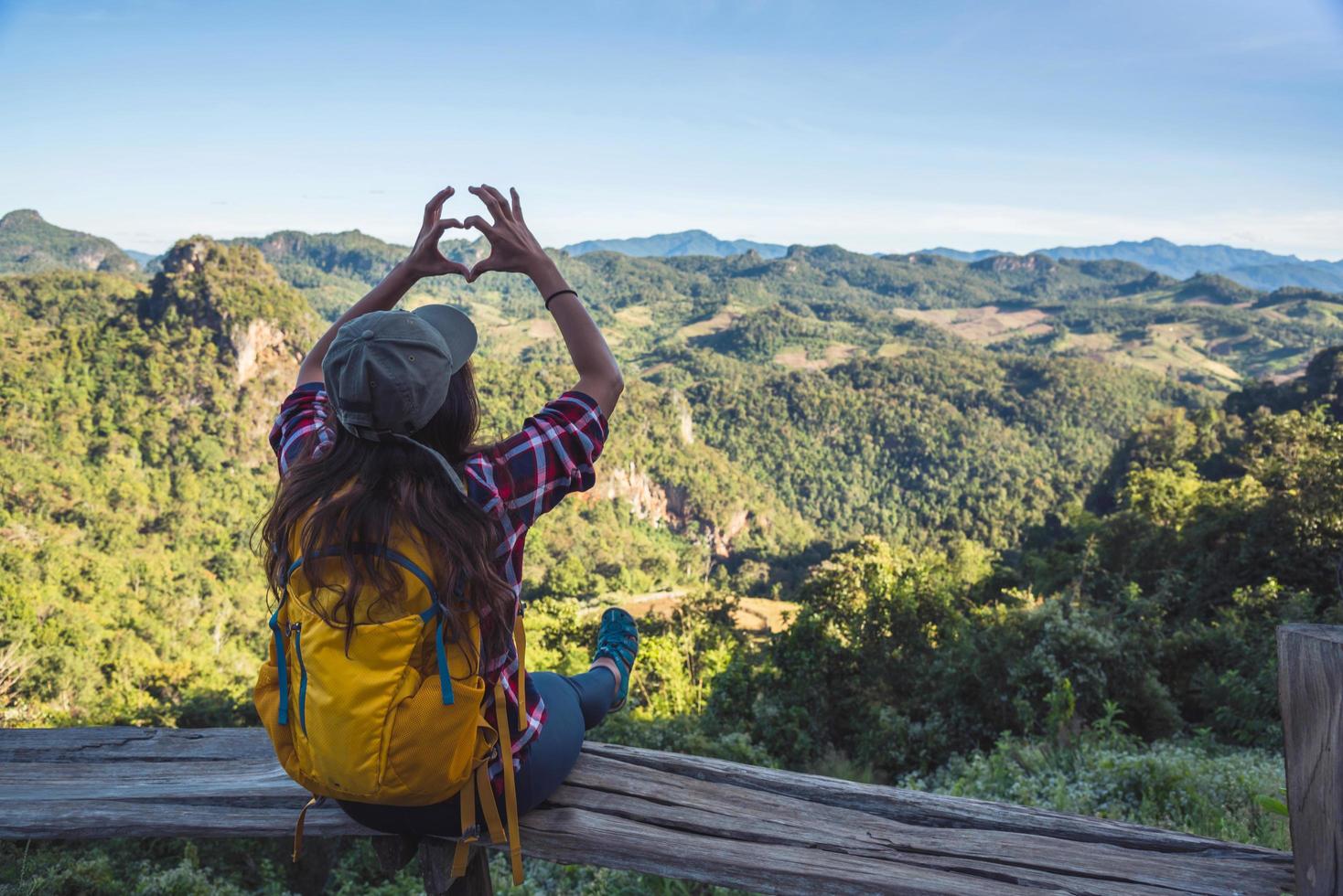 Joven turista con mochilas felices de viajar levantó la mano para hacer una forma de corazón y disfrutar del paisaje natural de la montaña. foto