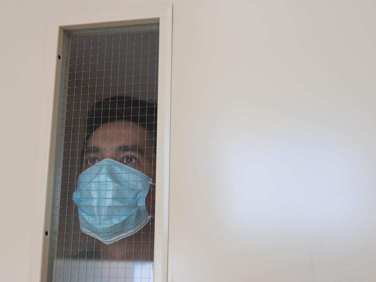 Lonely man in medical mask looking through the window. Isolation at home for self quarantine. Concept home quarantine, prevention COVID-19. Coronavirus outbreak situation photo