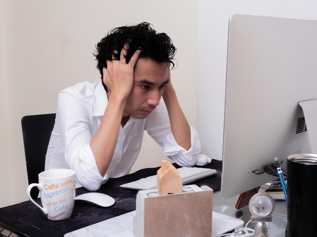 Serious Asian man is working with laptop in his apartment bedroom in concept of Work From Home and Work at Home photo