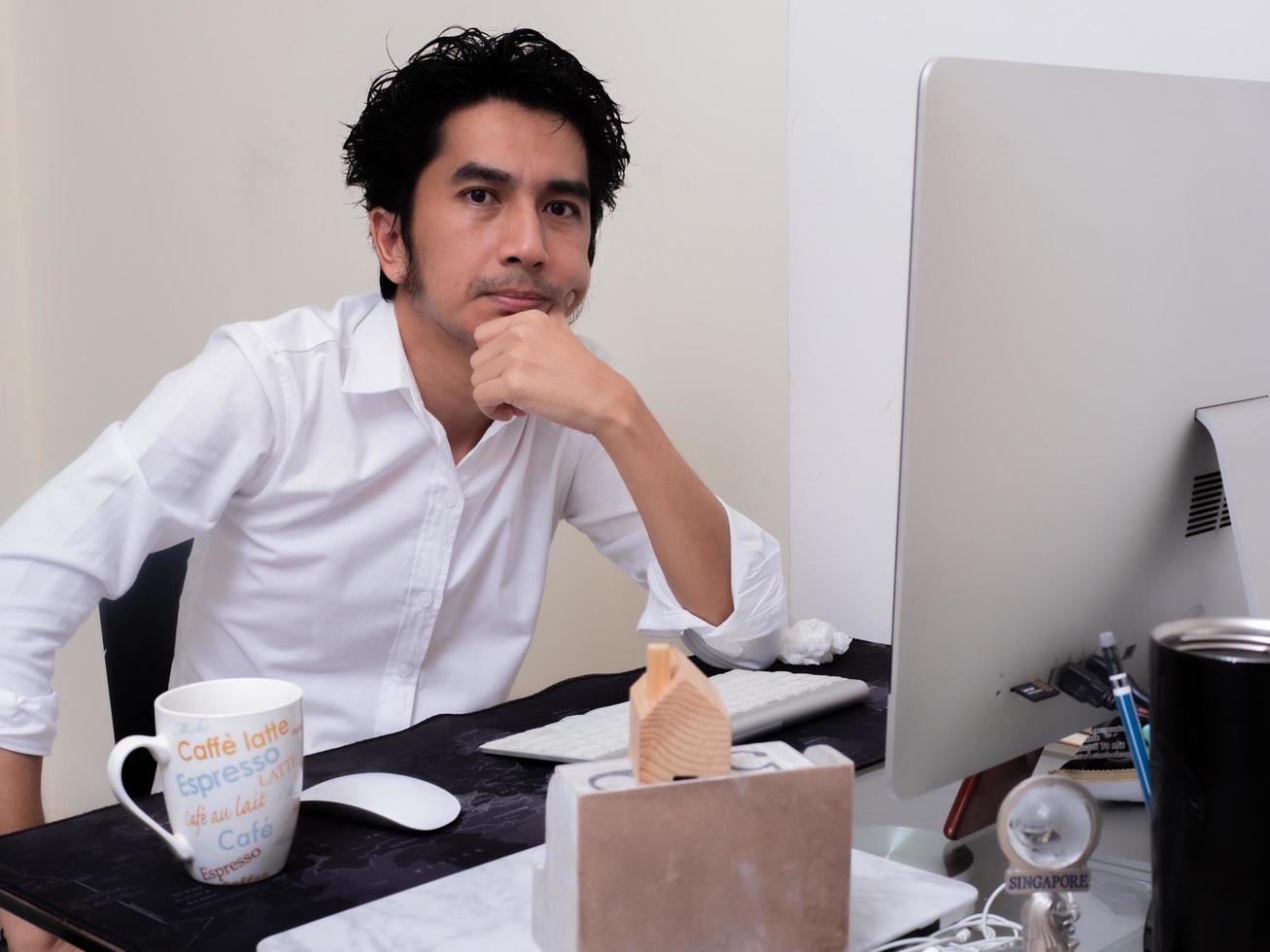 Serious Asian man is working with laptop in his apartment bedroom in concept of Work From Home and Work at Home photo