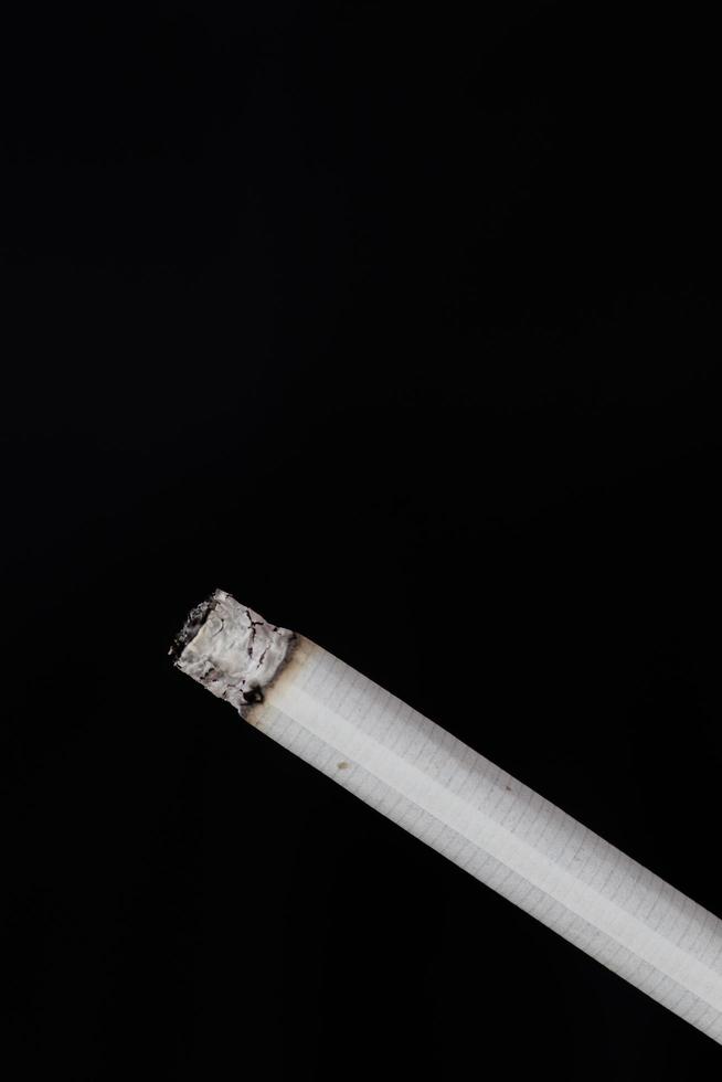 Burning cigarette with smoke on black background photo