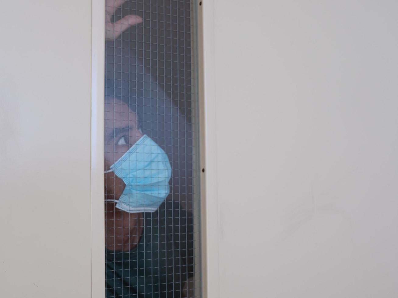 Lonely man in medical mask looking through the window. Isolation at home for self quarantine. Concept home quarantine, prevention COVID-19. Coronavirus outbreak situation photo