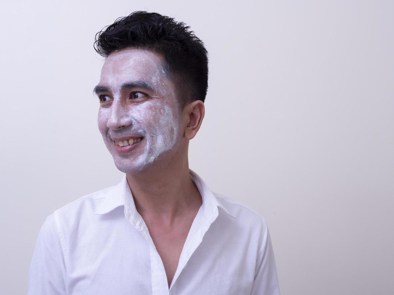 un joven apuesto asiático aplicándose crema en la cara con cara sonriente, concepto de cuidado de la piel foto