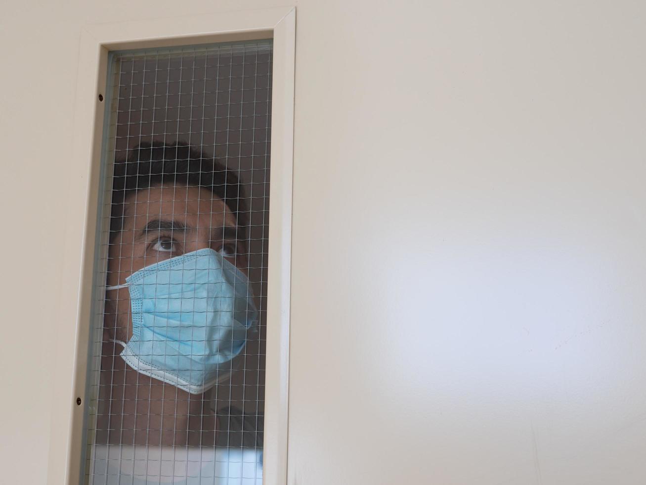 Lonely man in medical mask looking through the window. Isolation at home for self quarantine. Concept home quarantine, prevention COVID-19. Coronavirus outbreak situation photo