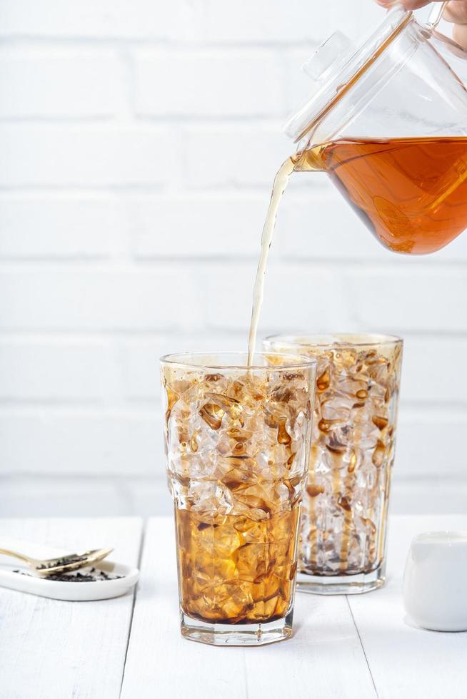 Making bubble tea, pouring blend milk tea into brown sugar pattern drinking glass cup on white wooden table background, close up, copy space photo