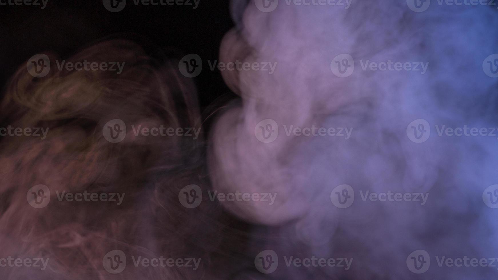 Conceptual image of multi-colored smoke isolated on dark black background and wooden table. photo