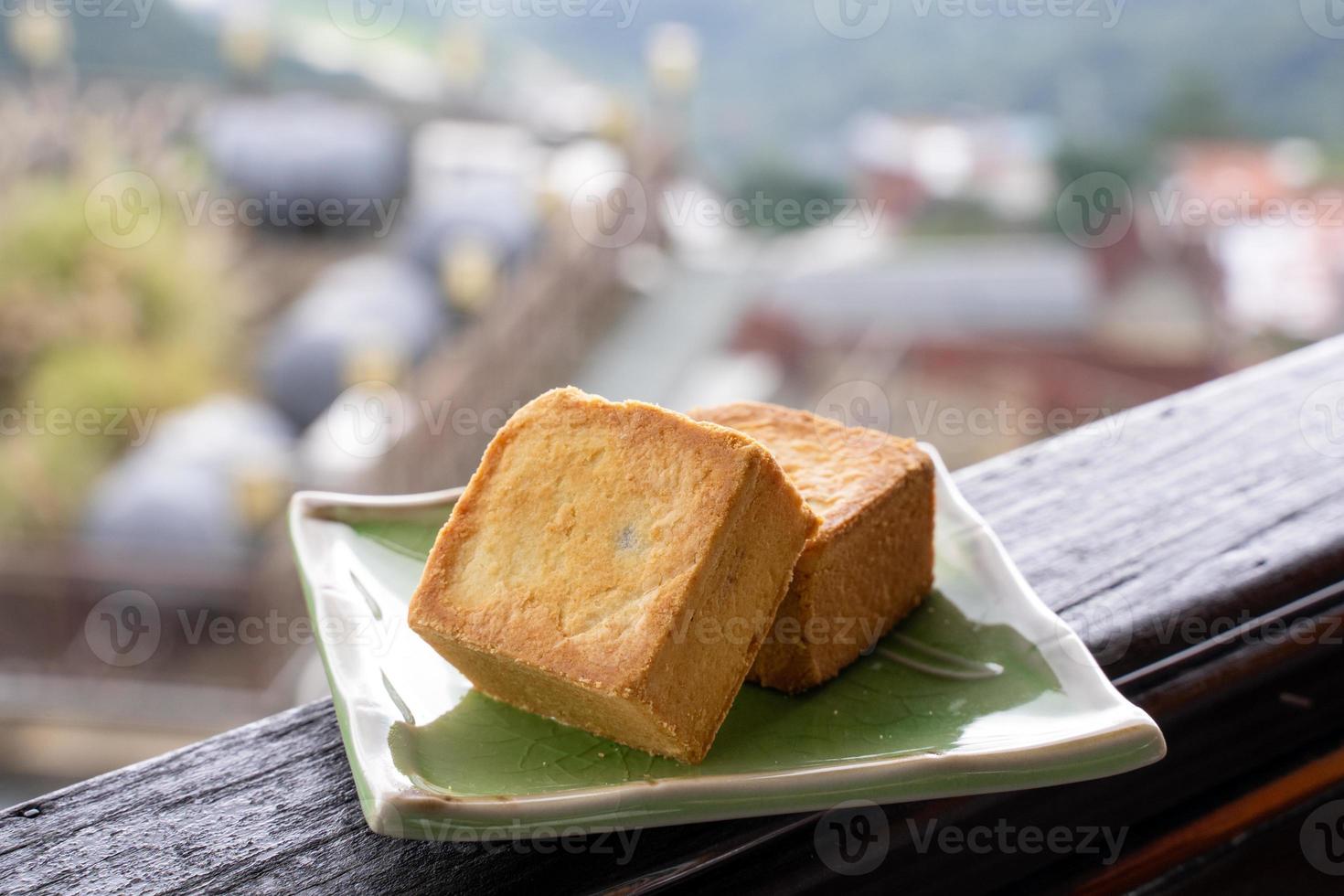 Delicious pineapple pastry in a plate for afternoon tea on wooden railing of a teahouse in Taiwan with beautiful landscape in background, close up. photo