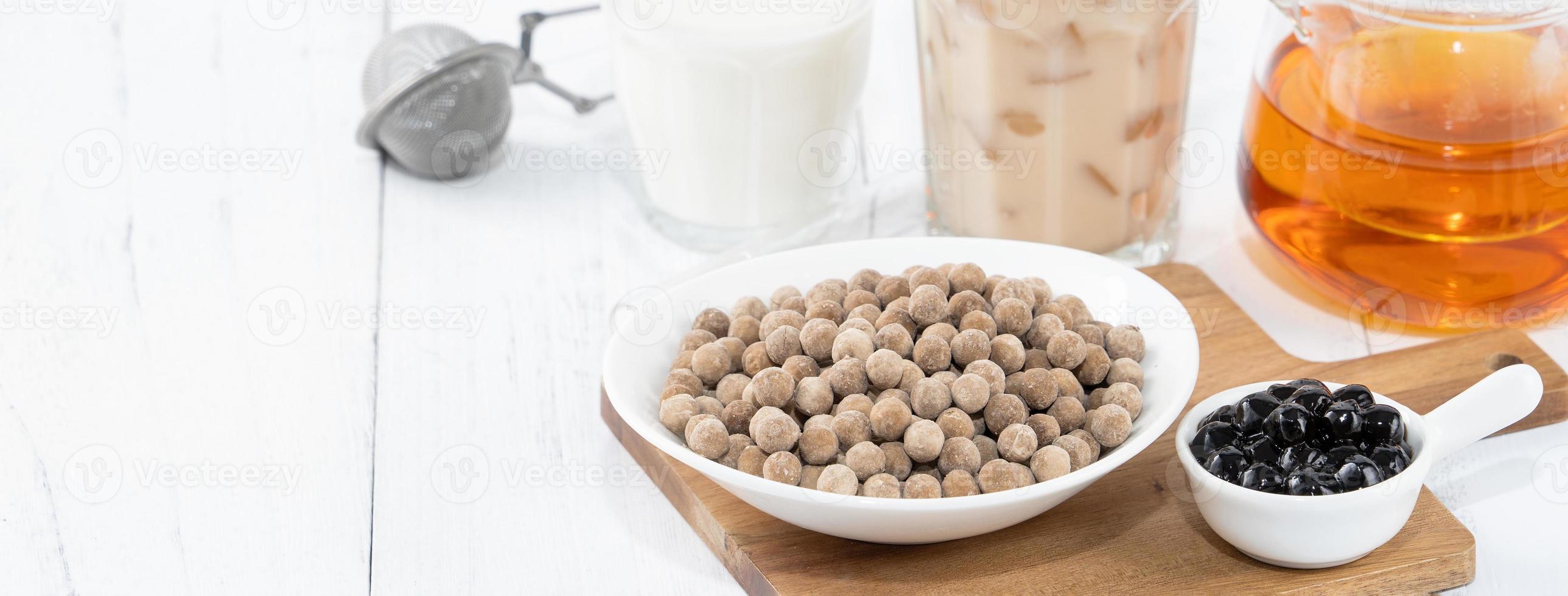 Bubble milk tea with tapioca pearl topping ingredient, famous Taiwanese drink on white wooden table background in drinking glass, close up, copy space photo