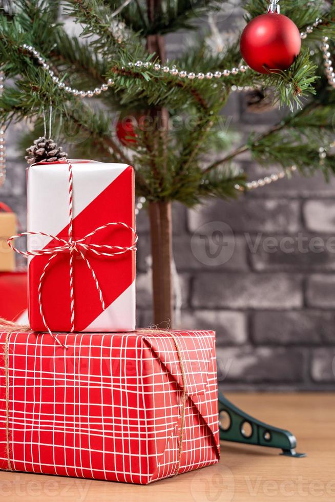 Decorated Christmas tree with wrapped beautiful red and white gifts at home with black brick wall, festive design concept, close up. photo