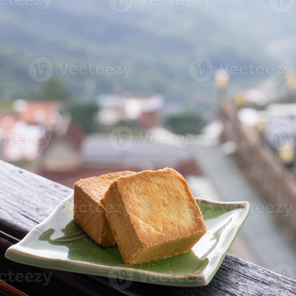 Delicious pineapple pastry in a plate for afternoon tea on wooden railing of a teahouse in Taiwan with beautiful landscape in background, close up. photo