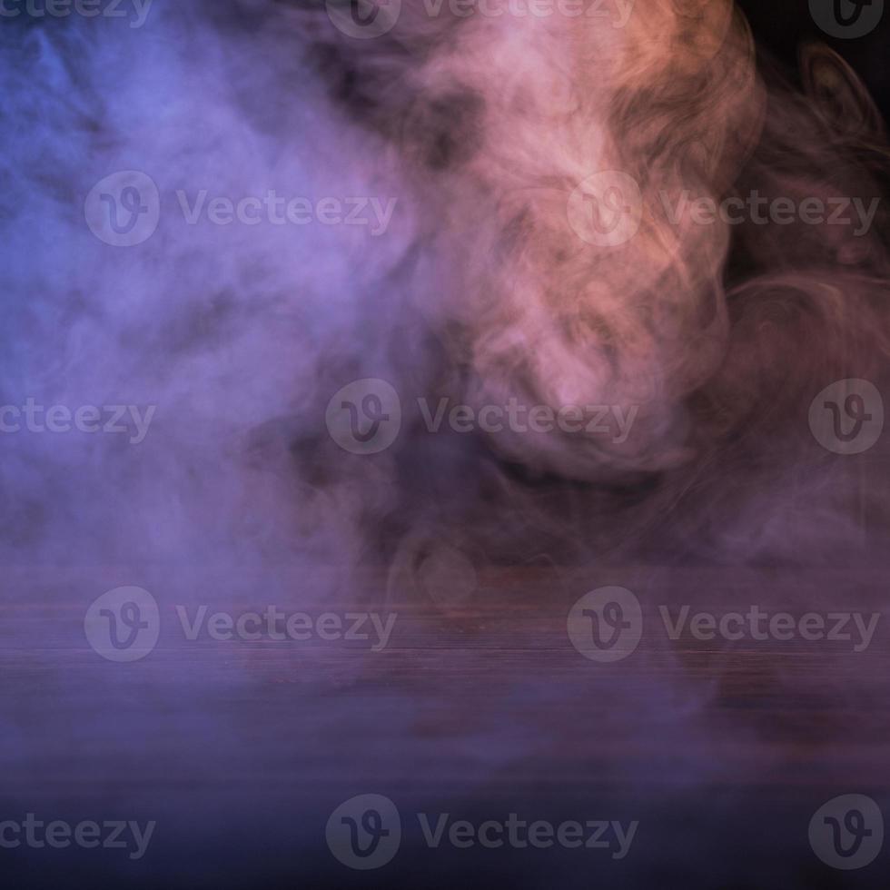 Conceptual image of multi-colored smoke isolated on dark black background and wooden table. photo