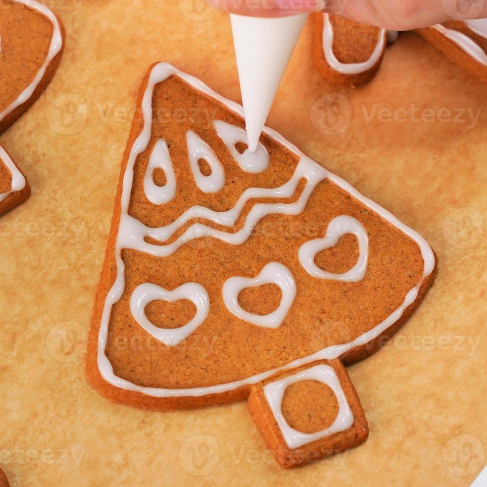 Young woman is decorating Christmas Gingerbread House cookies biscuit at home with frosting topping in icing bag, close up, lifestyle. photo