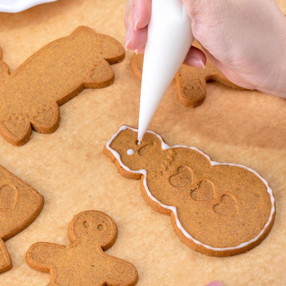 Young woman is decorating Christmas Gingerbread House cookies biscuit at home with frosting topping in icing bag, close up, lifestyle. photo