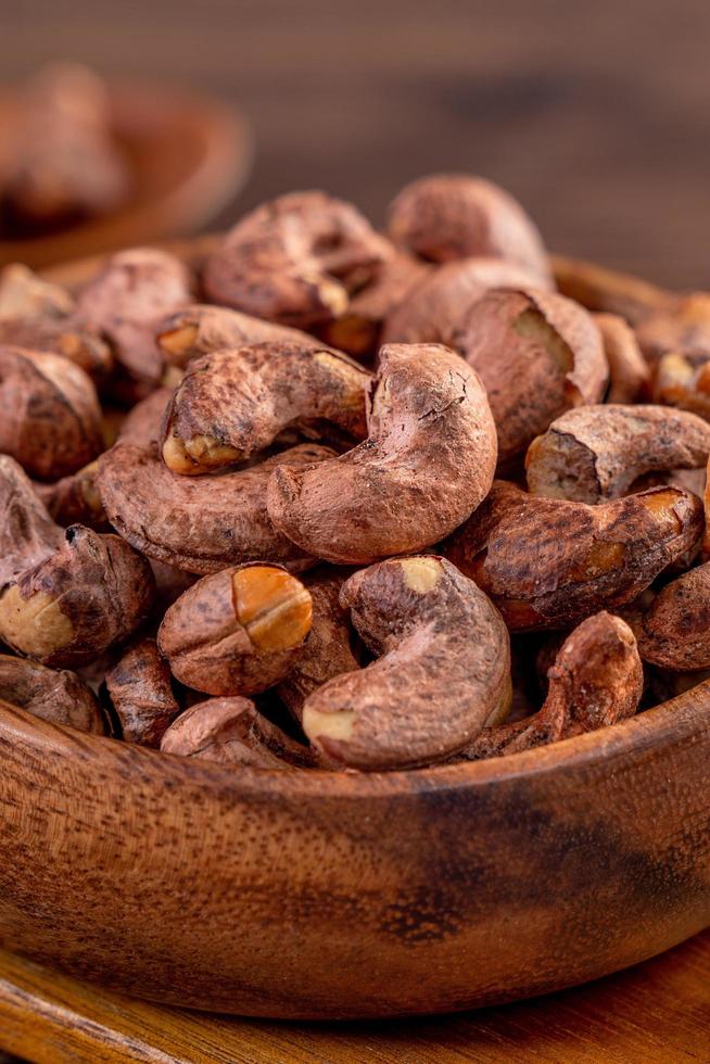 Cashew nuts with peel in a wooden bowl on wooden tray and table background, healthy raw food plate. photo