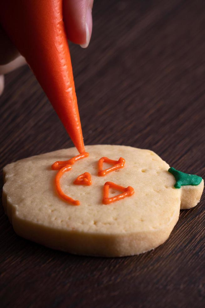 Close up of decorating cute Halloween pumpkin cookies with frosting in icing bag. photo