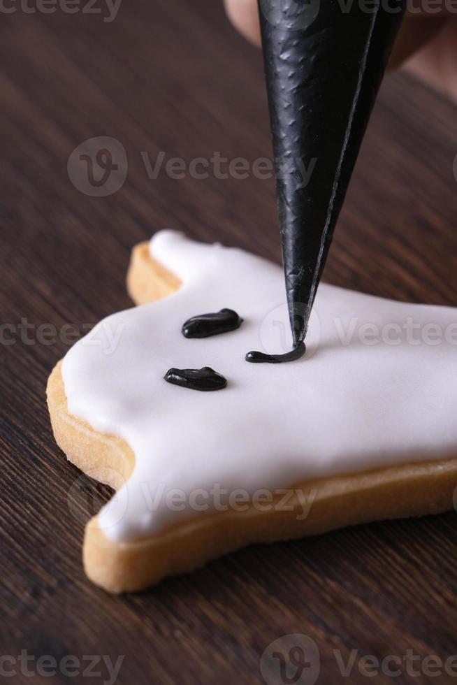 Close up of decorating cute Halloween ghost cookies with frosting. photo