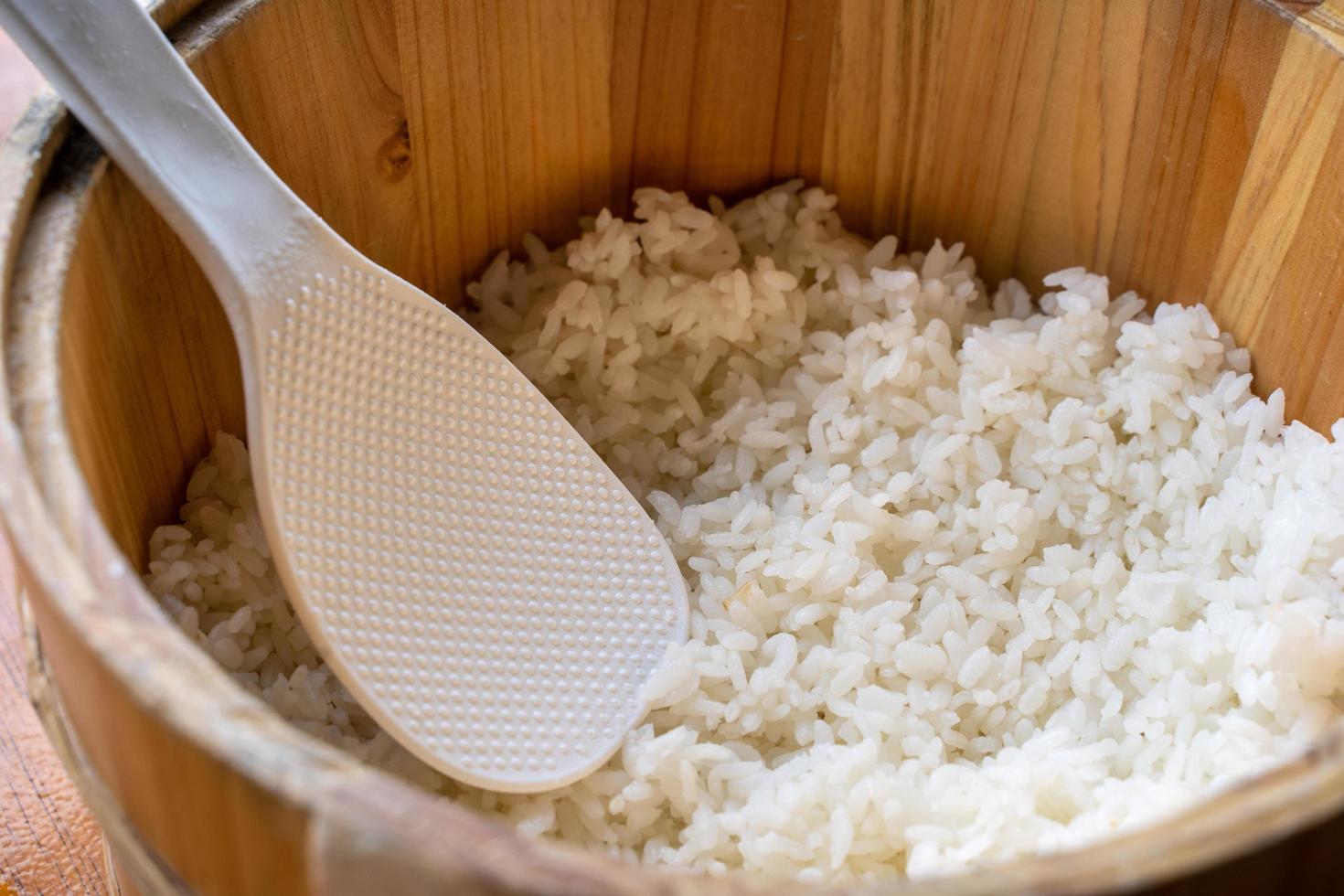 Delicious cooked plain rice in a big wooden bowl ready-to-eat with white rice spatula spoon at restaurant table, close up, lifestyle. photo