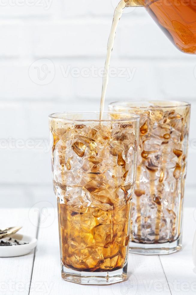 Making bubble tea, pouring blend milk tea into brown sugar pattern drinking glass cup on white wooden table background, close up, copy space photo