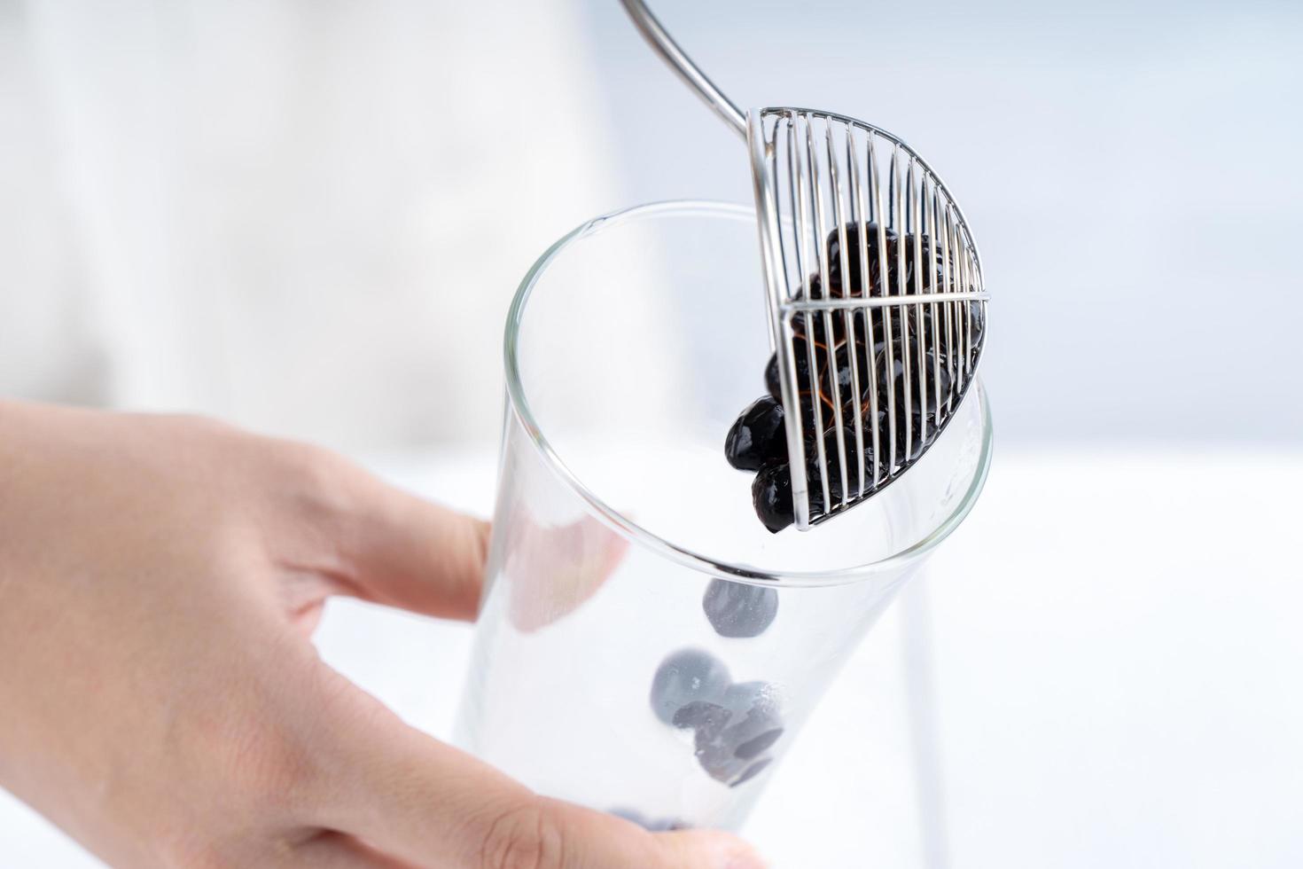 hacer té de burbujas, sacar y verter bolas de burbujas de perlas de tapioca con sabor a azúcar moreno cocido en una taza sobre fondo de mesa de madera blanca, cerrar, copiar espacio. foto