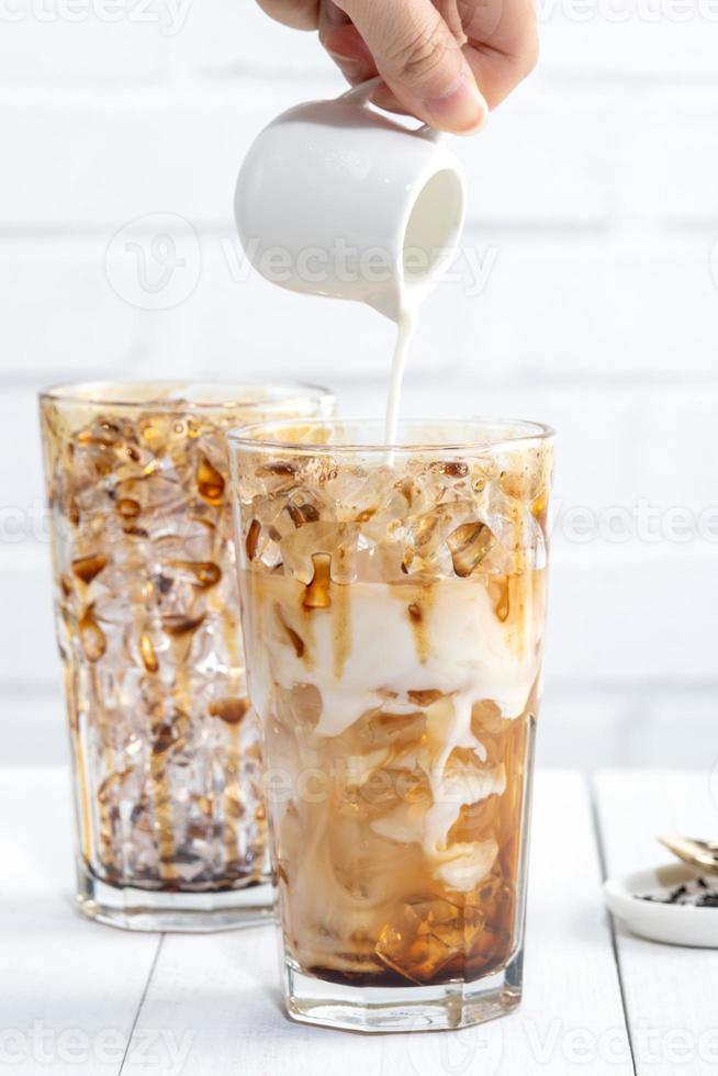 Making bubble tea, pouring blend milk tea into brown sugar pattern drinking glass cup on white wooden table background, close up, copy space photo