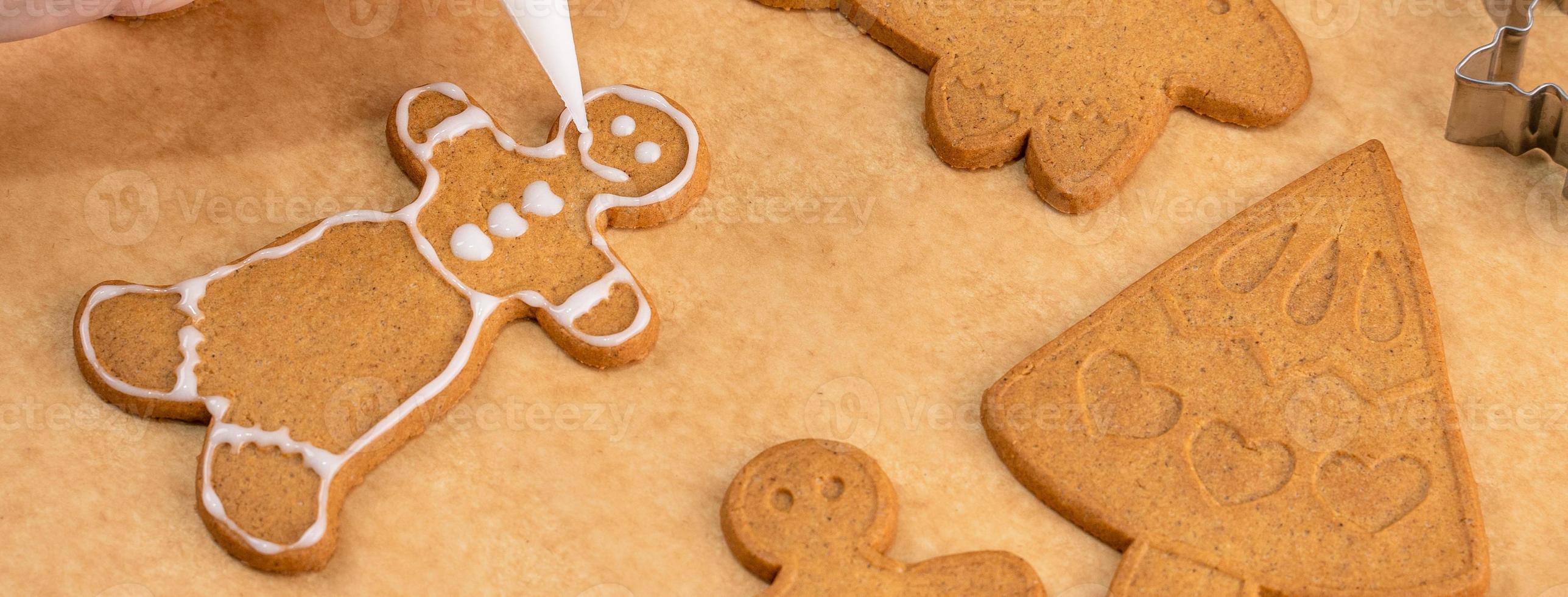 Young woman is decorating Christmas Gingerbread House cookies biscuit at home with frosting topping in icing bag, close up, lifestyle. photo