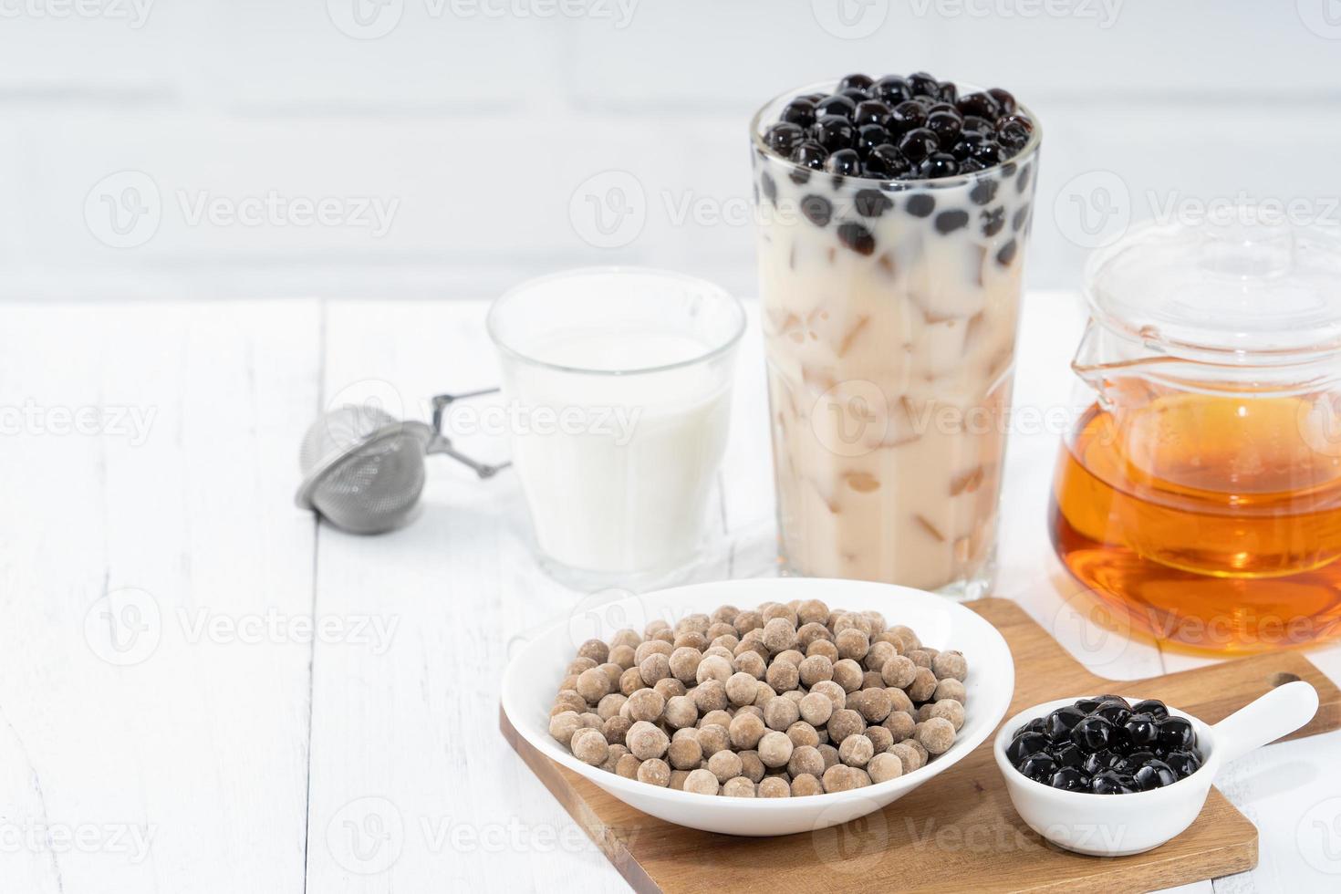 Bubble milk tea with tapioca pearl topping ingredient, famous Taiwanese drink on white wooden table background in drinking glass, close up, copy space photo