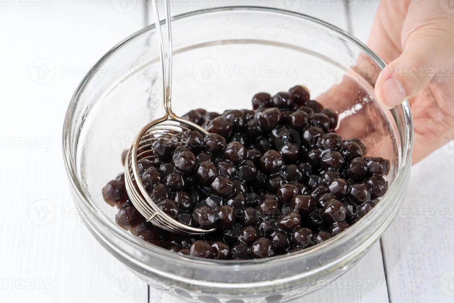 Making bubble tea, scoop and pour cooked brown sugar flavor tapioca pearl bubble balls into cup on white wooden table background, close up, copy space. photo